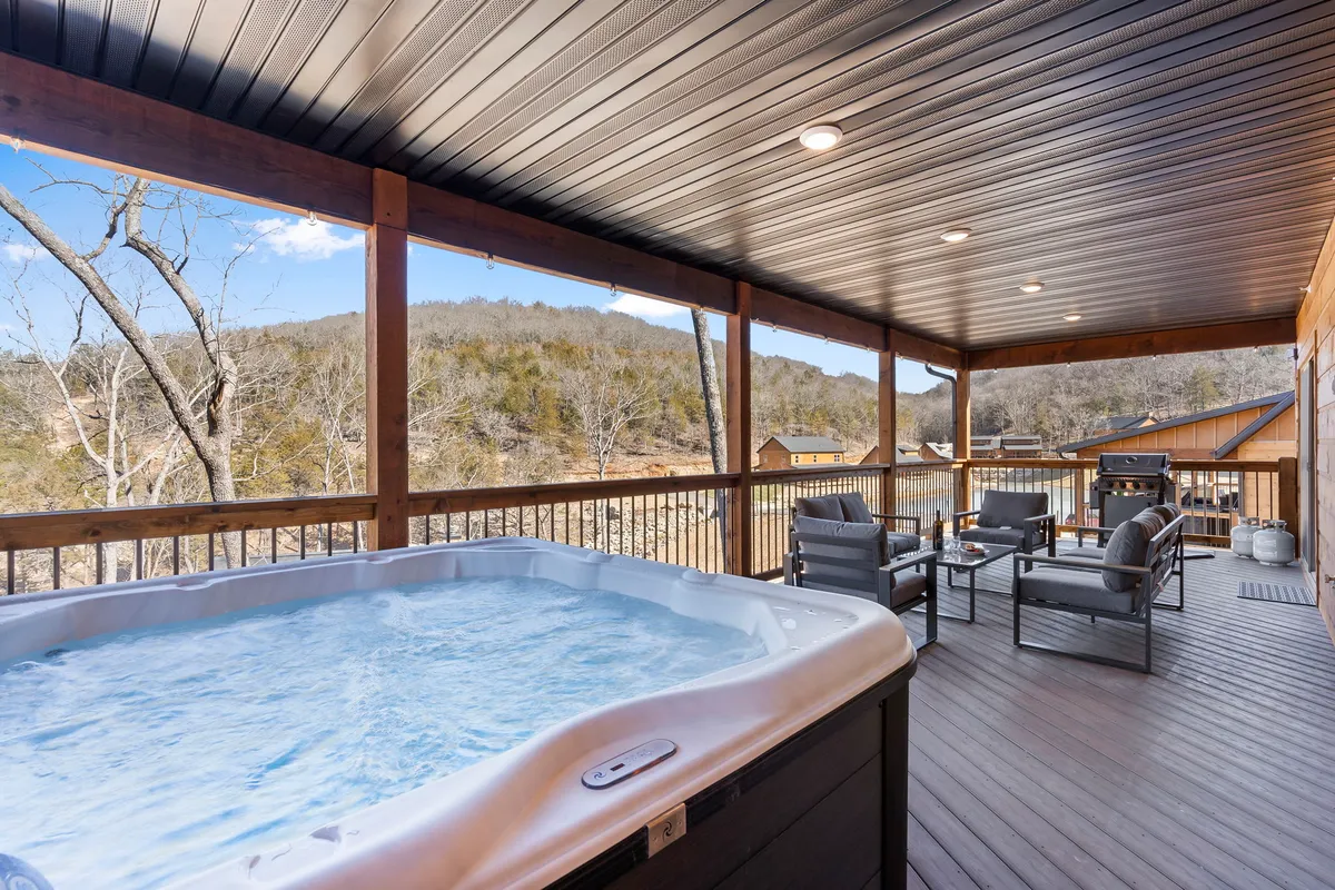 An inviting exterior scene showcasing a private hot tub and outdoor seating area with expansive mountain views in the background. The hot tub is surrounded by natural greenery and the tranquil patio space is perfect for relaxation or small gatherings.