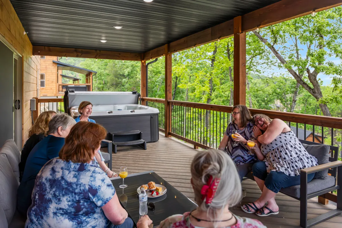 A group of friends is gathered in an outdoor hot tub, surrounded by natural greenery. Refreshments are set on a nearby table, creating a lively atmosphere of relaxation and camaraderie after a day of activities.