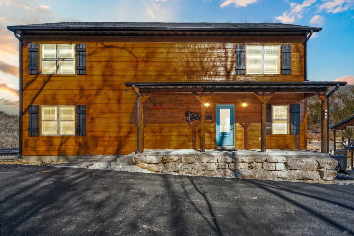 The image features a wooden facade with a welcoming front porch, a vibrant blue door, and stone steps. The porch invites relaxation and suggests a hospitable environment, with a touch of rustic charm ideal for pets and families.
