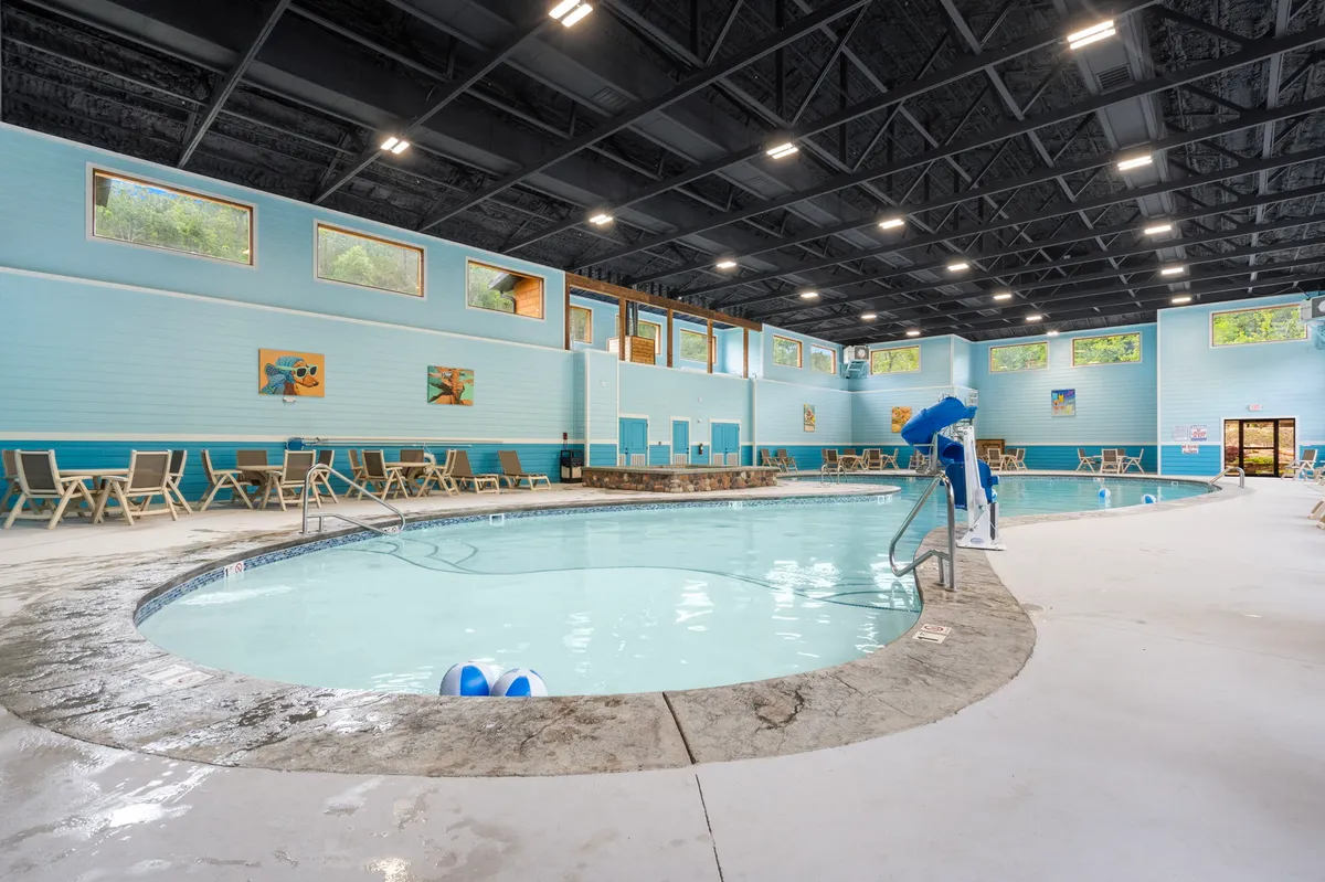 A bright, interior view of the resort's indoor swimming pool area, complete with lounge chairs, abundant natural light, and colorful wall art. The scene captures families and children enjoying the pool year-round.