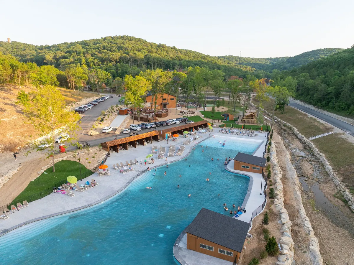 A vibrant exterior shot of a swimming pool surrounded by tall trees and wooden structures. Lounge chairs are set up around the pool, and the area exudes a welcoming atmosphere for gatherings, relaxation, and fun under the sun. The pool is large enough for group activities, and the natural surroundings suggest a private yet communal experience.