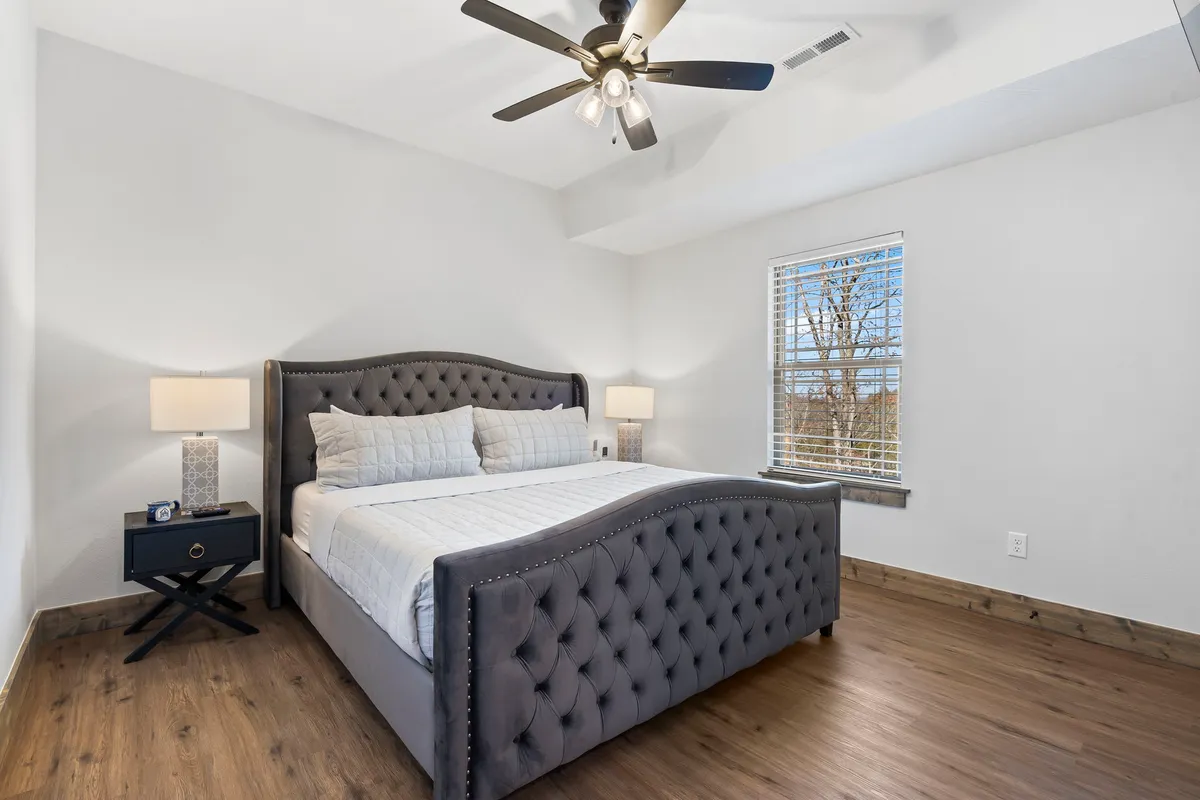 This image depicts a king-sized tufted bed with a nightstand and lamp beside it, bathed in natural light coming through the window. The overall ambiance is serene and restful, emphasizing comfort and a private sanctuary for guests.