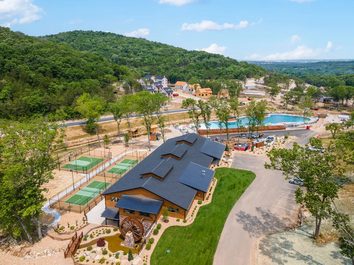 This exterior image showcases multi-sport courts, a swimming pool, a wooden building, and landscaped gardens. The courts are clearly visible and designed for activities like tennis and basketball, while the pool and seating areas suggest room for relaxation and gatherings.