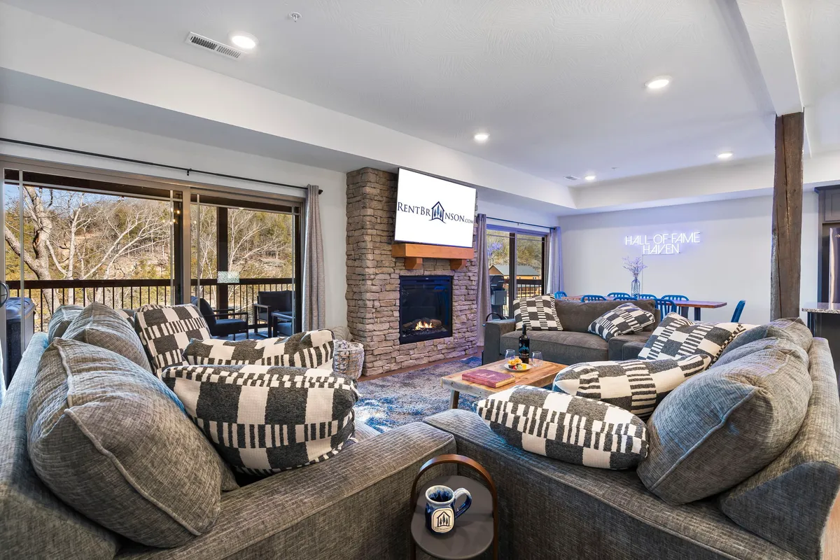 This image features a spacious living room centered around a grand stone fireplace, a large sectional sofa, a television screen, and a coffee table. The seating arrangement is oriented to encourage gathering and conversation, while the fireplace exudes warmth and coziness.