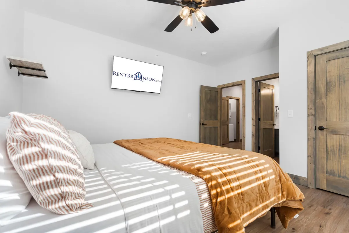 A cozy bedroom featuring a bed with an orange blanket, a wall-mounted television, and wooden doors. The setup emphasizes relaxation and entertainment, highlighting individual TVs and a comfortable atmosphere.