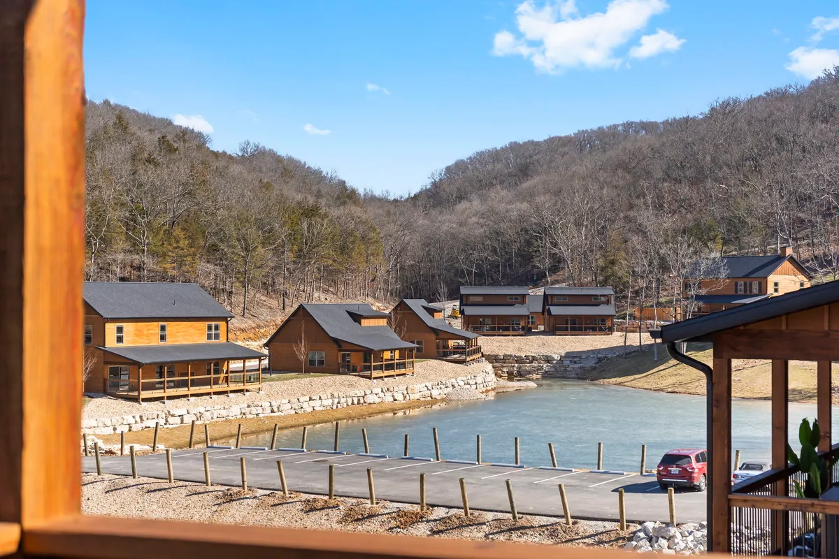 This image captures several rustic cabins nestled by a tranquil lake, set against a backdrop of rolling mountains and lush greenery. The scene is serene, inviting guests to enjoy fishing, hiking, boating, or simply relaxing by the water—activities highlighted in the retreat's offering.