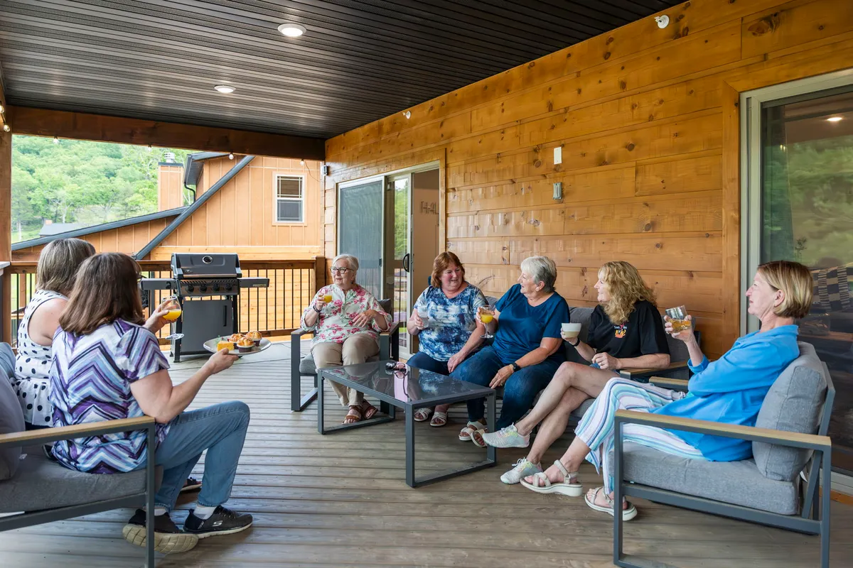 A group of people enjoys an outdoor seating area beside a grill, engaging in conversation and sharing refreshments. The mood is joyful, capturing a sense of celebration and togetherness after outdoor activities.