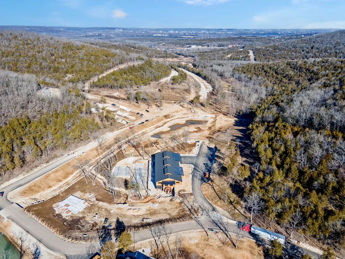A newly constructed building sits amid a lush natural landscape, with fresh wood siding and a winding road leading to its entrance. The scene is tranquil, highlighting the pristine architecture and its seamless integration with nature. The building's newness is evident, and the surrounding area appears open, with some visible signs of ongoing development.