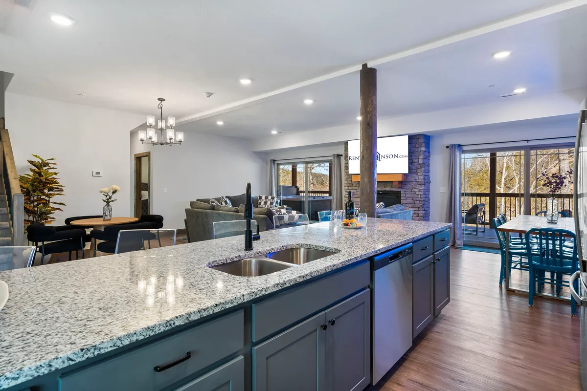 An open-concept space seamlessly connecting a kitchen island, dining area, and living space with large windows that showcase resort views. The room is bathed in natural light and designed for flow between cooking, dining, and socializing.