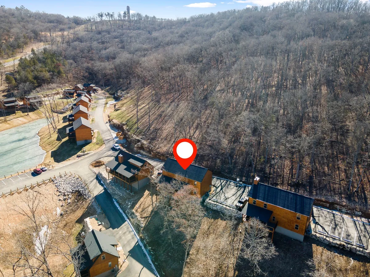 A cluster of wooden cabins lines a winding road bordered by trees, set in a peaceful natural environment. The open area and expansive greenery suggest opportunities for outdoor walks and exploration.