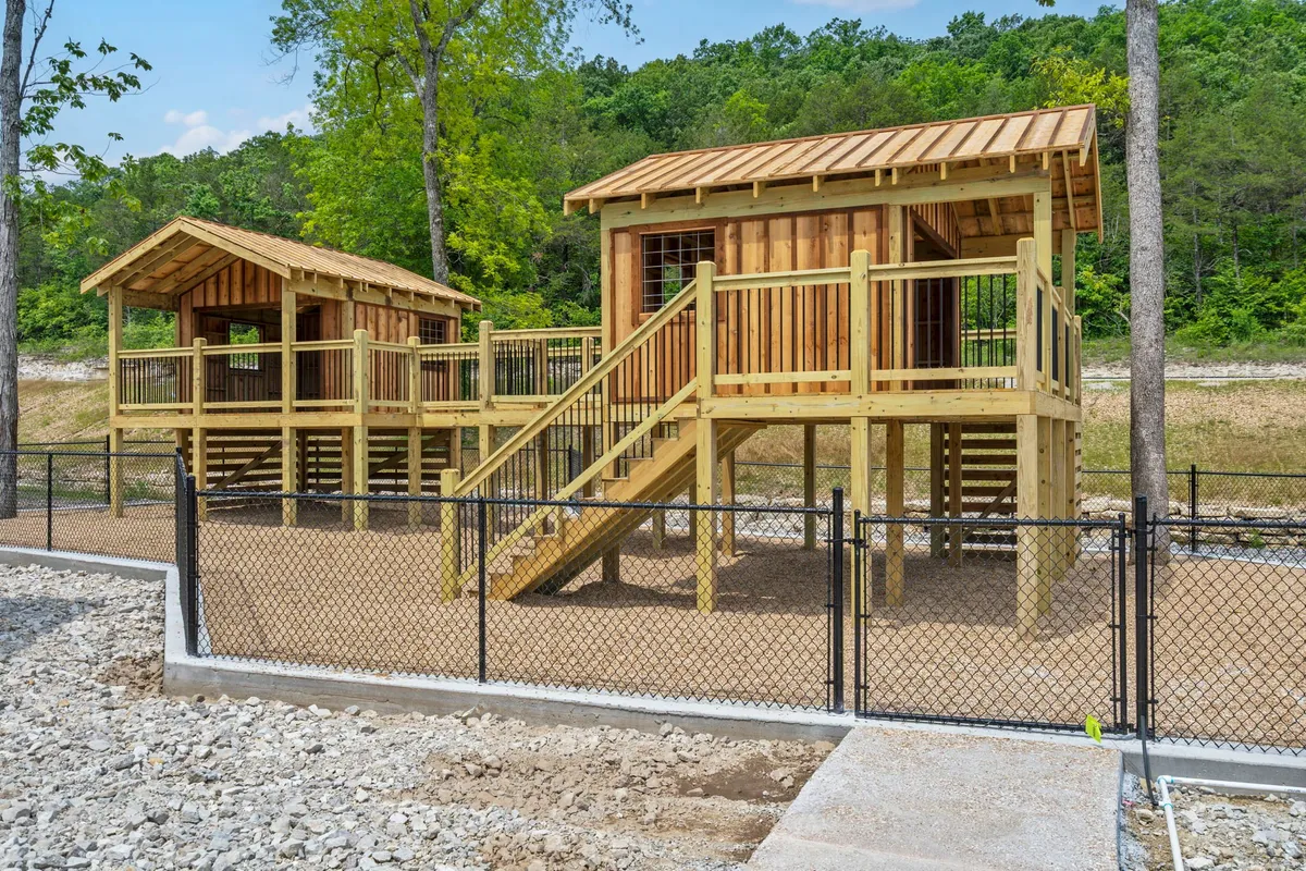 This image showcases two wooden playhouses set within a fenced area, surrounded by lush greenery. The playful structures and open space evoke a family- and pet-friendly atmosphere, suggesting a safe area for pets and children to enjoy the outdoors.